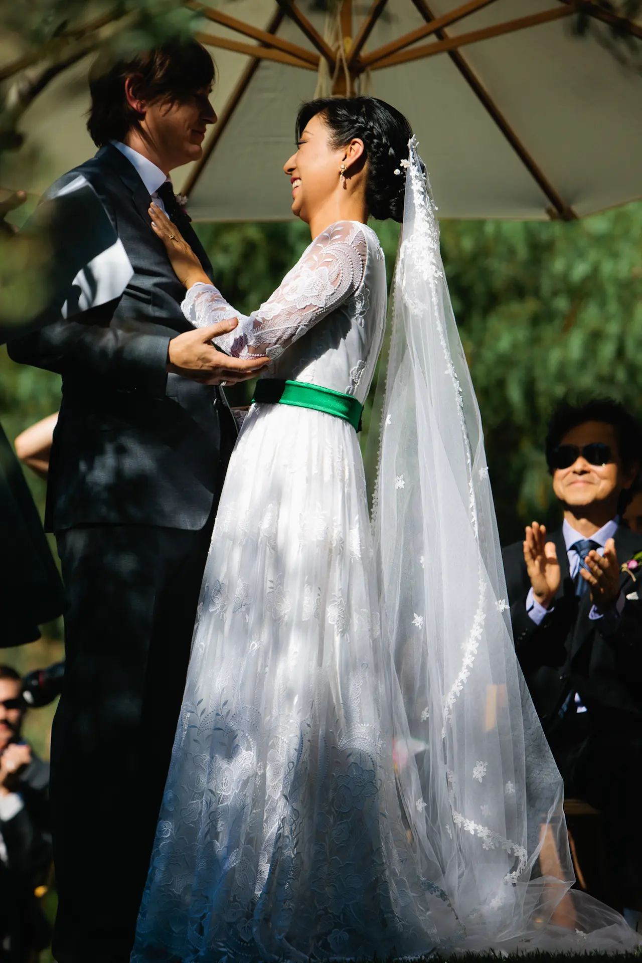 A bride and groom smiling at each other under an umbrella during their ceremony